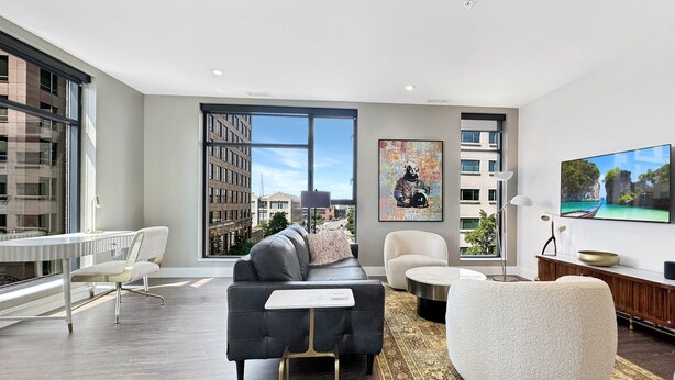 A modern living room with a large window, a black sofa, a white armchair, and a flat-screen TV. - Rare Luxury: Apartment with Unparalleled Elegance (Rochester)