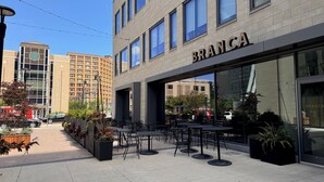 A modern building with the name 'BRANCA' on the facade. It features outdoor seating with tables and chairs, surrounded by planters with greenery. - Rare Luxury: Apartment with Unparalleled Elegance (Rochester)