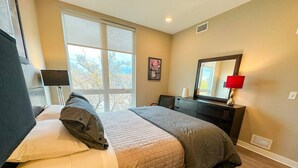 A bedroom with a bed, a desk, a chair, a window, and a mirror. - Bright, Colorful & Convenient 1-Bedroom Apartment (Rochester)