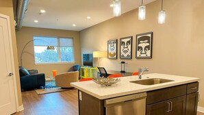 A modern kitchen with a stainless steel dishwasher, a large island with a sink, and a dining area with a table and chairs. - Bright, Colorful & Convenient 1-Bedroom Apartment (Rochester)