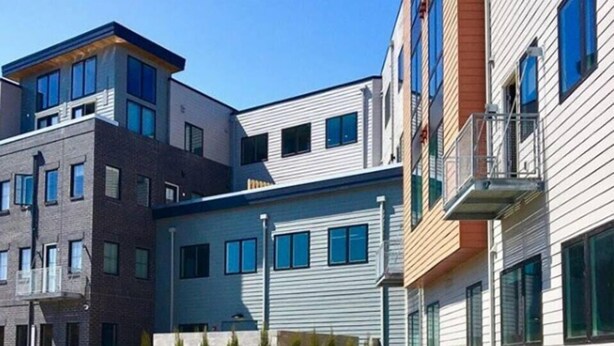 A modern multi-story residential building with a central courtyard, featuring a curved pathway and small trees. - Bright, Colorful & Convenient 1-Bedroom Apartment (Rochester)
