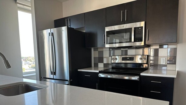 A modern kitchen with stainless steel appliances, black cabinets, and a white countertop. - Tower280 LUXE One-Bedroom Corner Unit with Views! (Rochester)