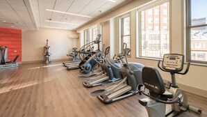 Une salle de sport équipée de plusieurs tapis de course et de plusieurs appareils elliptiques, dotée de grandes fenêtres et d’un plancher en bois.