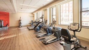 Une salle de sport équipée de plusieurs tapis de course et de plusieurs appareils elliptiques, dotée de grandes fenêtres et d’un plancher en bois.