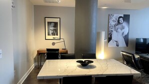 Un espace repas moderne avec une table en marbre, des chaises noires, un centre de table composé d’un vase noir, un luminaire suspendu et une grande colonne cylindrique.