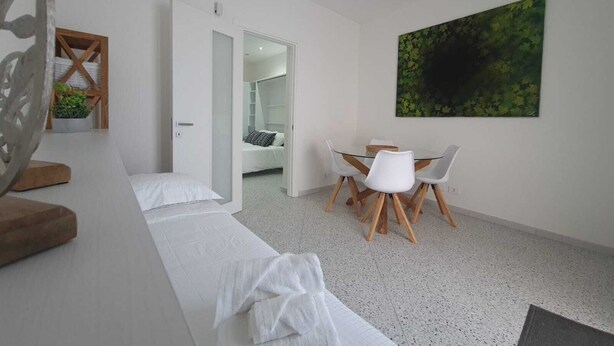 A modern bedroom with a bed, a small table with chairs, a large painting, and a door leading to a bathroom. - Private House 14 Palermo (Palermo)