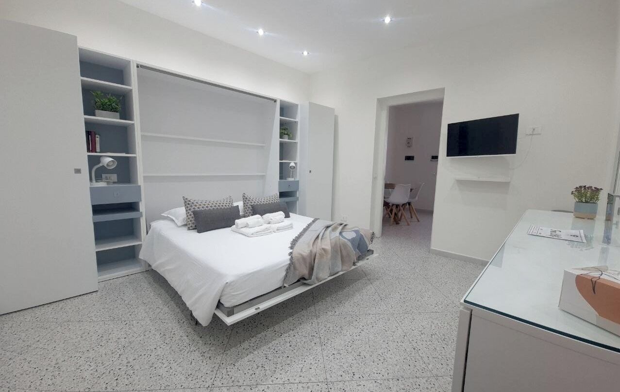 Une chambre moderne avec un lit, des étagères intégrées, un téléviseur et une table en verre.