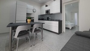 A modern kitchen with white cabinets, a black countertop, and a dining area with two chairs and a table. - Private House 14 Palermo (Palermo)