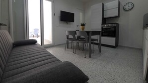 A modern living room with a sofa, a dining area with chairs, a TV mounted on the wall, and a kitchen with an oven. - Private House 14 Palermo (Palermo)