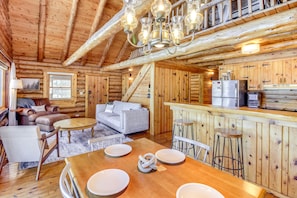 Interno di una baita di legno con zona pranzo, cucina e soggiorno.