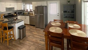 A modern kitchen with white cabinets, a stainless steel refrigerator, and a dining area with a wooden table and chairs. - Beautiful Mountainside Escape (Anchorage)