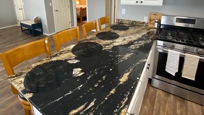A kitchen with a black marble countertop, wooden chairs, a stainless steel stove, and white cabinets. - Beautiful Mountainside Escape (Anchorage)