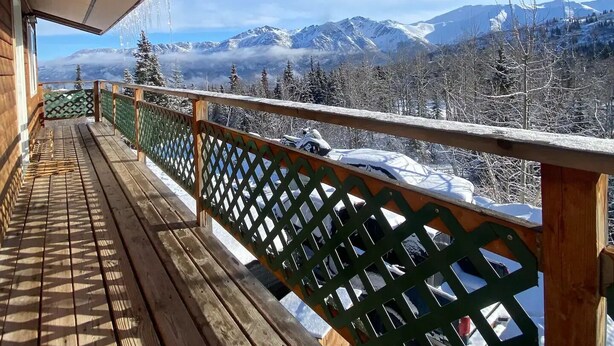 A wooden deck with a green lattice railing overlooking a snowy mountain landscape. - Beautiful Mountainside Escape (Anchorage)