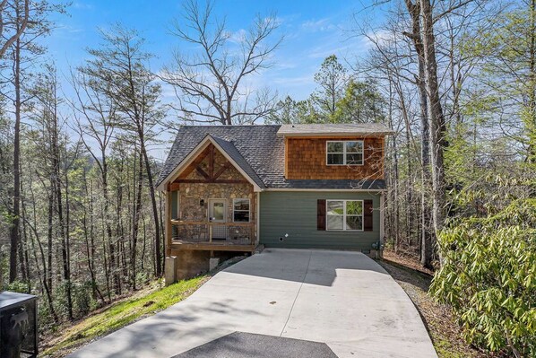 A cabin with a stone foundation, a wooden upper level, and a porch. - Bobcat Den (Gatlinburg)
