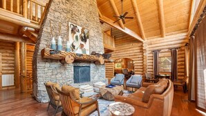 A log cabin interior with a stone fireplace, wooden furniture, and a high ceiling with exposed beams. - Legend Crest Lodge (Sevierville)