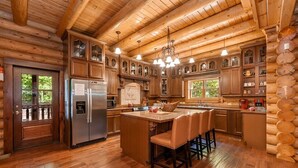 A log cabin kitchen with wooden cabinets, a central island, and a stainless steel refrigerator. - Legend Crest Lodge (Sevierville)