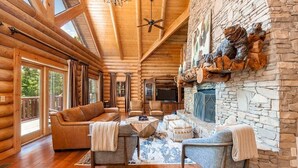 A log cabin interior with a stone fireplace, wooden ceiling beams, and a cozy seating area. - Legend Crest Lodge (Sevierville)