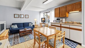 Un salon moderne avec un canapé, une table basse et une table à manger. Il y a également un coin cuisine avec des meubles en bois et une fenêtre.