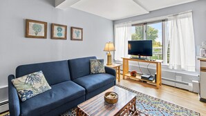Un salon avec un canapé bleu, un téléviseur posé sur un meuble en bois et des œuvres d’art encadrées accrochées au mur.