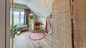 Une pièce avec un plafond en pente, un grand miroir, une chaise, un radiateur et une plante en pot.