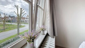 Une pièce avec une fenêtre donnant sur la rue, un radiateur et deux plantes en pot sur le rebord de la fenêtre.