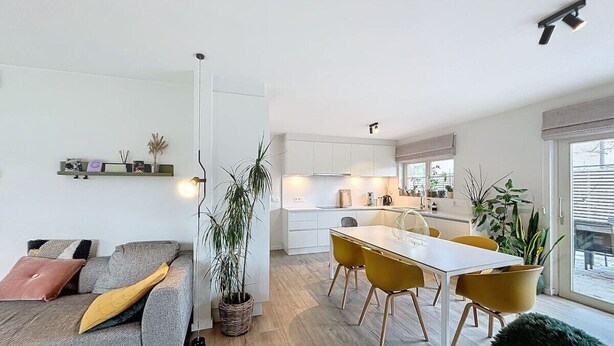 Un salon moderne avec un canapé, une table à manger entourée de chaises jaunes et un coin cuisine doté de meubles blancs.