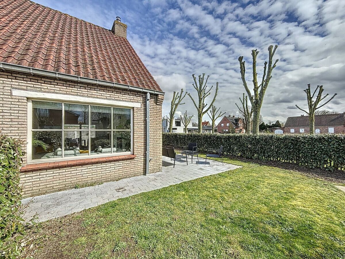 Une maison avec une façade en briques, de grandes fenêtres et une terrasse dallée.