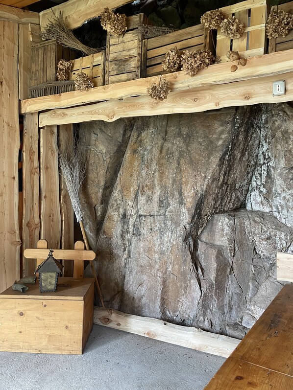 A rustic interior with wooden walls, a stone-like textured wall, and a wooden shelf with dried flowers.