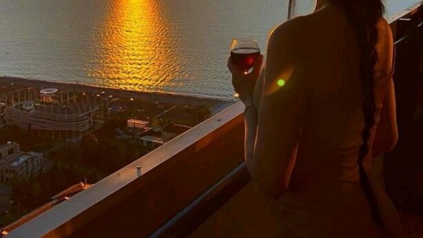 Une vue sur le coucher de soleil depuis un balcon donnant sur une étendue d’eau, avec une silhouette de ville en arrière-plan.