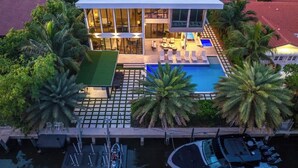 Ein modernes Haus mit Pool, Terrassemöbeln und einem Steg mit Booten.