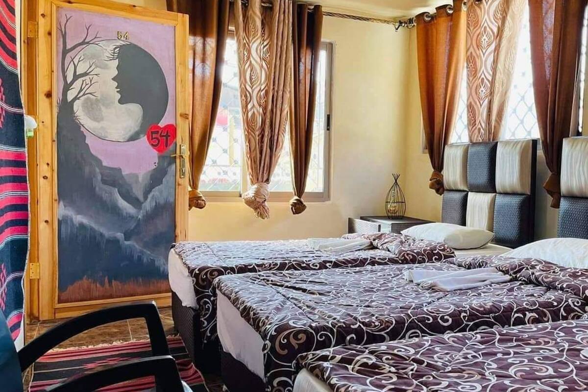 A hotel room with two beds, a painting on the wall, and curtains.