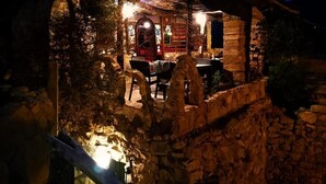 Un edificio rústico de piedra con un patio cubierto, muros de piedra y una pérgola de madera.