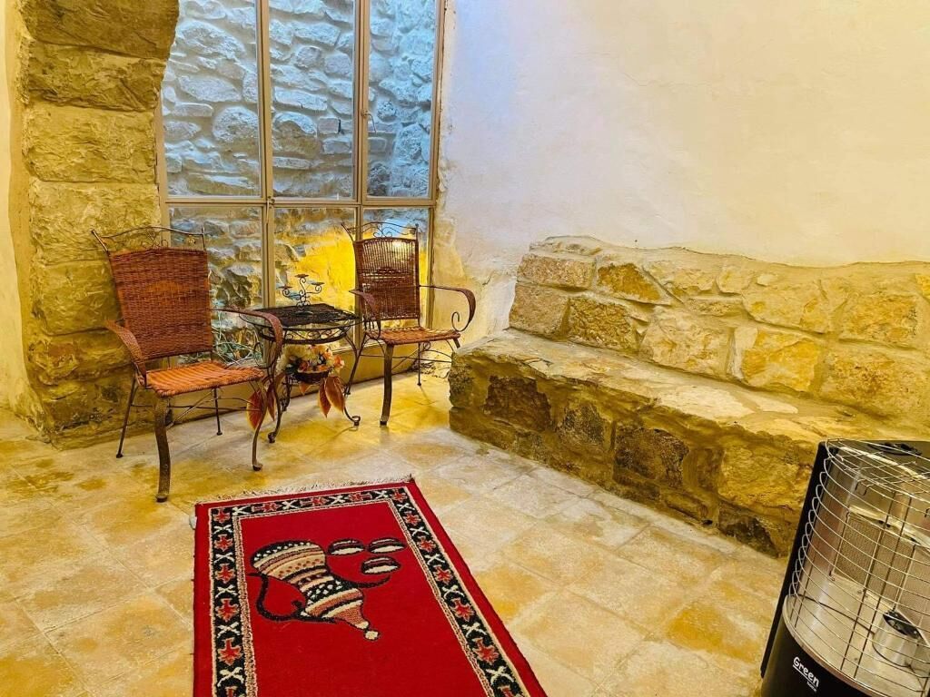 A cozy corner with a stone wall, a window, wicker chairs, a small table, and a red rug.