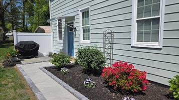 A house with a covered grill, a pathway, and flower beds with various flowers.