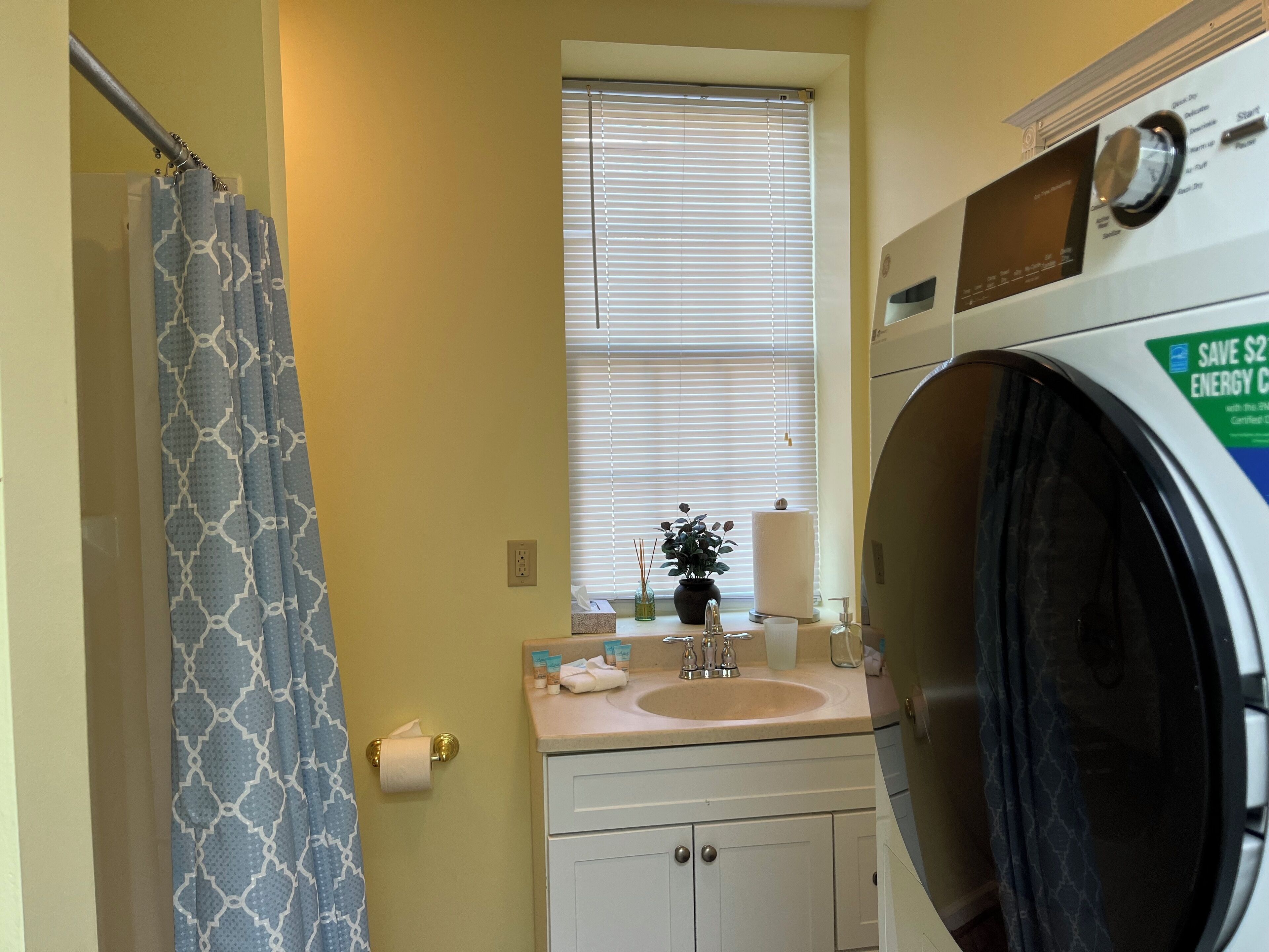 Una sala de lavandería con lavadora, una ventana con persianas, un lavabo y un dispensador de toallas.