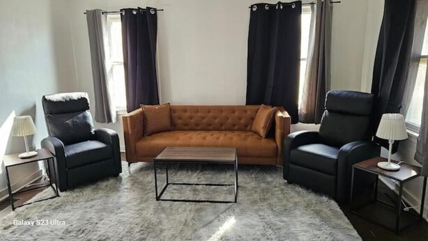 A living room with a brown sofa, two black armchairs, a coffee table, and a rug. - Get More Bang For Your Buck! (Wichita)