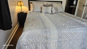 A neatly made bed with patterned bedding, a bedside lamp, and a TV on a stand. - Get More Bang For Your Buck! (Wichita)