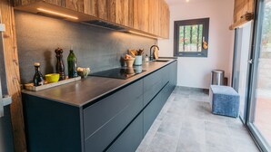 A modern kitchen with wooden cabinets, a built-in island, and a large window. - The Getaway, your temporary home away from home (Pals)