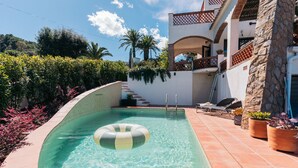 A swimming pool with a floating ring, a stone wall, and a staircase leading to a balcony. - The Getaway, your temporary home away from home (Pals)