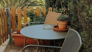 Een ronde metalen tafel met twee stoelen, een bloempot en een glazen schaal.