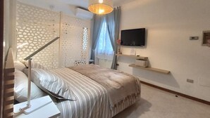 Een slaapkamer met een bed, een aan de muur bevestigde televisie, een plafondlamp en een raam met gordijnen.