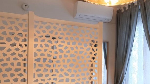 Een kamer met een decoratieve scheidingswand, een airconditioning en een raam met gordijnen.