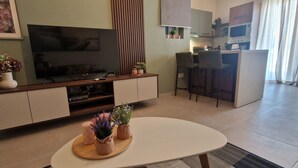 Een moderne woonkamer met een flatscreen-tv, een eethoek met barstoelen en een keuken met een magnetron en oven.