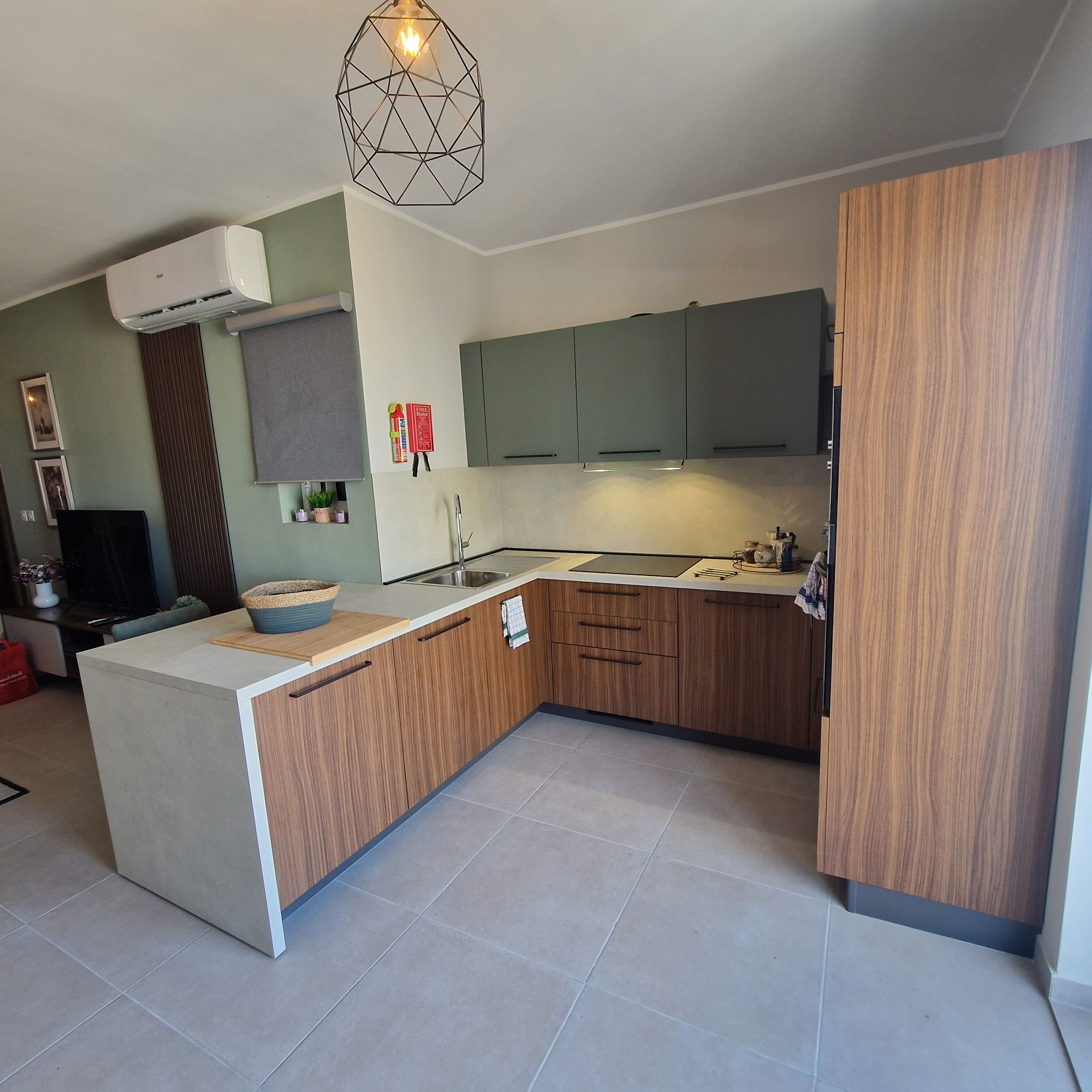 Een moderne keuken met een centraal eiland, houten kasten, een inbouwoven en een hanglamp.