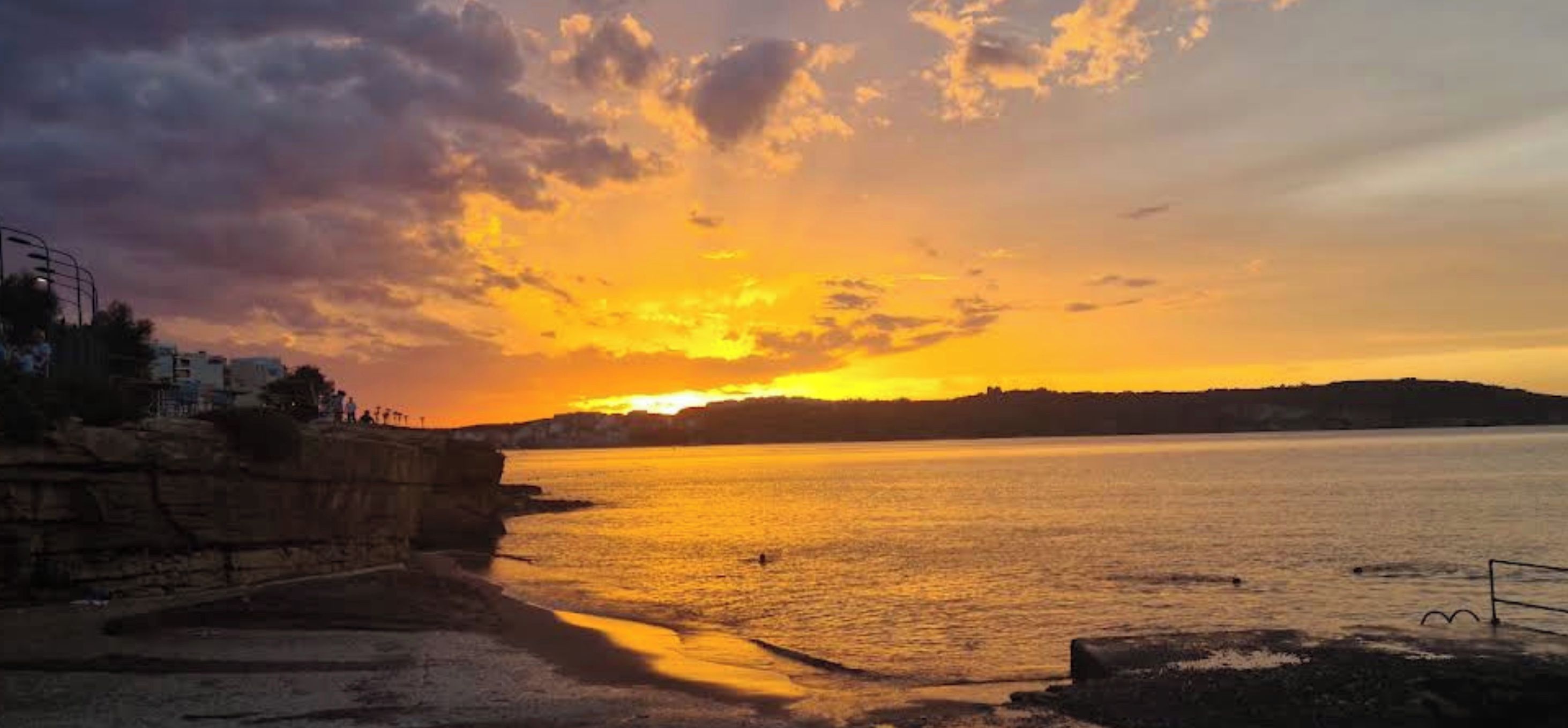A sunset over a body of water with a rocky shoreline and a distant landmass.