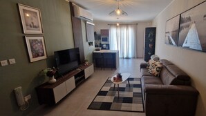 Een moderne woonkamer met een flatscreen televisie, een bank, een salontafel en een keuken op de achtergrond.