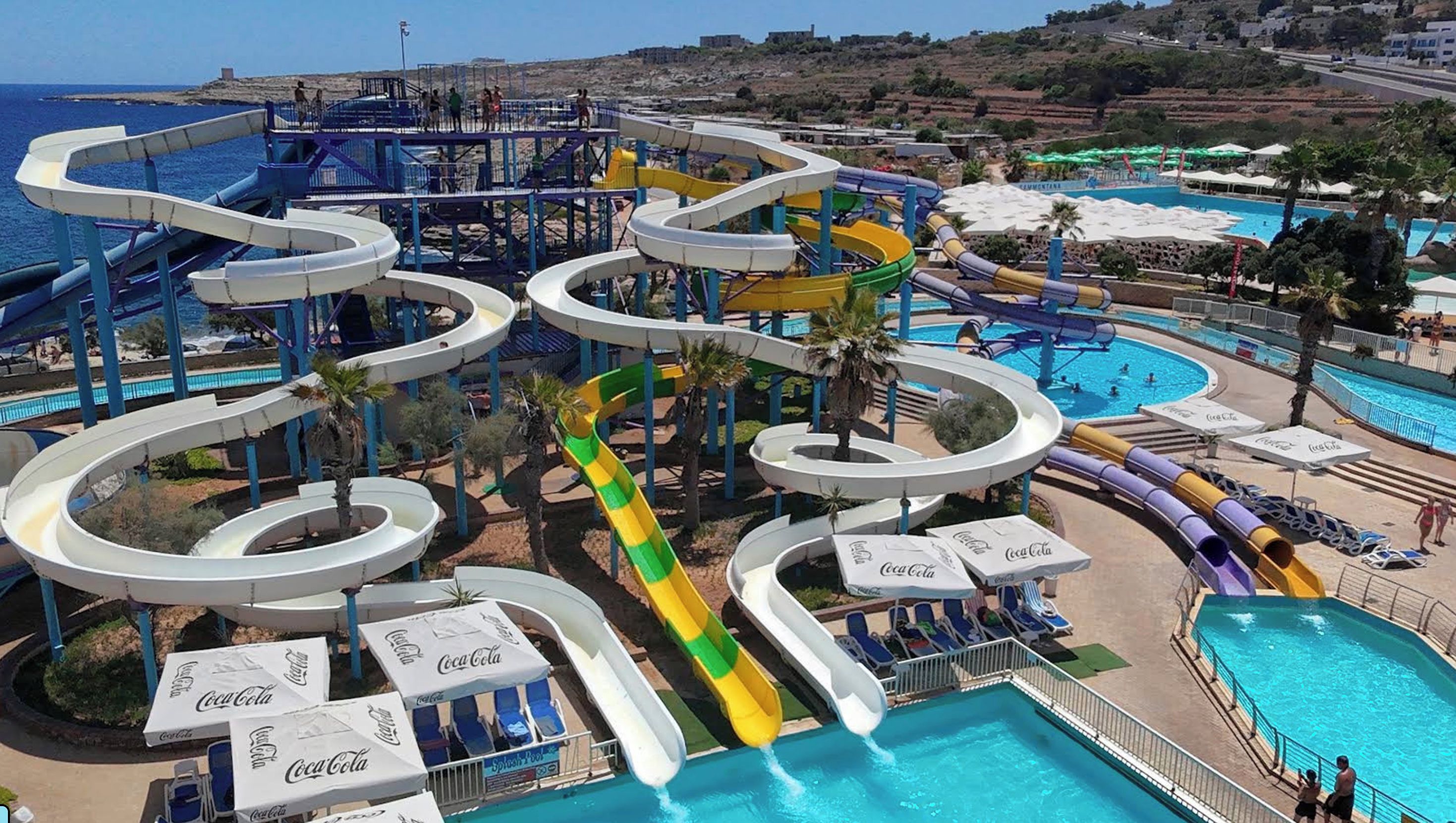 Un parc aquatique doté de nombreux toboggans et de plusieurs piscines, entouré de palmiers et offrant une vue sur la plage.