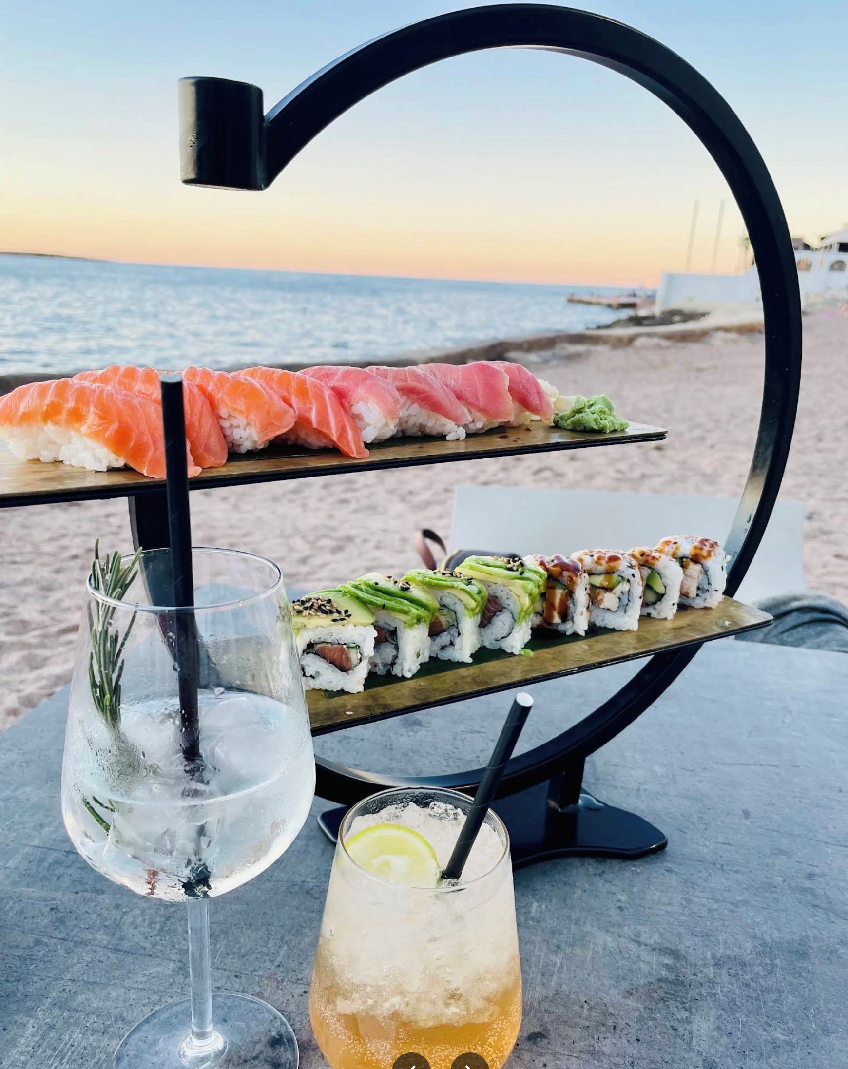 Una mesa con sushi y bebidas en un lugar frente al mar.