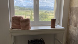 A window seat with a view of a green landscape, a white shelf with baskets, and a wicker basket on the floor. - Gîtes Chez Prune Entièrement Rénové Avec Piscine Privée (Rasteau)