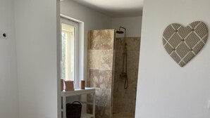 A bedroom with a striped bed, a white nightstand, a shower area, and a heart-shaped wall decoration. - Gîtes Chez Prune Entièrement Rénové Avec Piscine Privée (Rasteau)